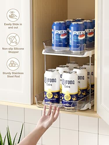 Hand reaching for cans in a kitchen cabinet organizer with Pepsi and Corona Extra.